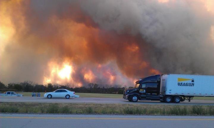 Vehicles stopped on the highway, large smoke clouds rising in the distance.